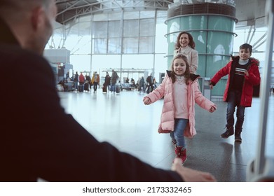 Happy Excited Woman With Her Kids Running To Her Husband In The Airport Arrivals Terminal Waiting Room, Meeting Him After His Business Trip. Long-awaited Family Reunion Concept