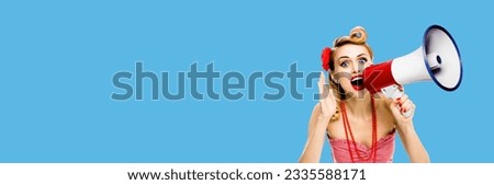 Happy excited woman holding mega phone and shout something. Blond girl in pin up style with wide open mouth, over blue color background with copy space. Female model in retro vintage studio ad concept