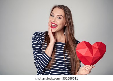 Happy excited woman with red polygonal paper heart shape with expression of surprise