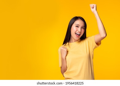 Happy excited young asian female with raised hands celebrating success Portrait cheerful asian woman with raised fists and smile face Attractive girl get happy, enjoy life yellow background copy space