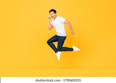 Happy Excited Young Asian Man Jumping Isolated On Yellow Studio Background