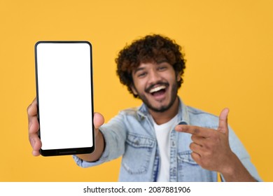 Happy excited young indian man showing smartphone pointing at big mockup white blank phone template screen isolated on yellow background presenting cellphone mobile offer application ads concept.