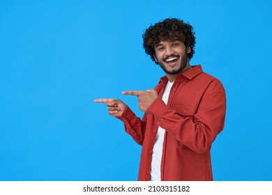 Happy excited young indian man looking at camera pointing aside with fingers hand gesture at copy space advertising new promotion, presenting sale offer standing isolated on blue background. - Powered by Shutterstock
