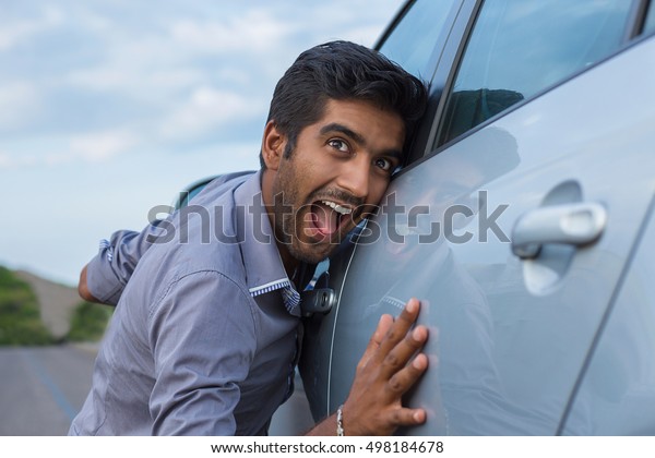 Happy excited young indian man driver embracing petting\
his car outdoors. Green energy biofuel electric environment\
friendly new car concept.\
