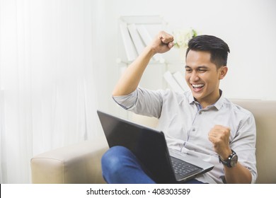 happy excited young man with laptop at home sitting on a couch
