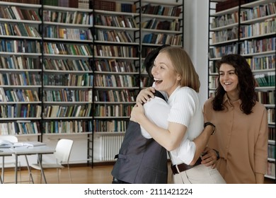 Happy Excited Young University Students Hugging In Library. Cheerful College Girl And Guy, High School Friends Meeting In Campus, Greeting, Embracing Each Other, Laughing, Smiling, Feeling Joy