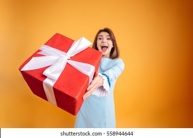 Happy Excited Young Woman Giving You Gift Box Over Yellow Background