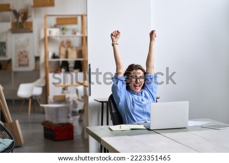 Happy excited young woman student or employee, office worker winner using laptop computer celebrating goal achievement winning online getting good news in email raising hands feeling euphoric.