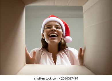 Happy Excited Young Woman In X Mas Santa Hat Receiving Parcel With Christmas Gift, Looking Inside Carton Box With Smile, Joy, Excited, Amazement, Opening Package. Low Angle, Bottom View Portrait