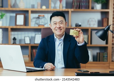 Happy And Exciting Asian Banking Businessman Looking At Camera And Smiling, Working In Classic Office, Holding Thumbs Up, And Offering Gold Bank Credit Card