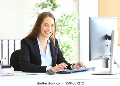 Executivo feliz olha para a câmera no escritório com as mãos no teclado do computador no escritório