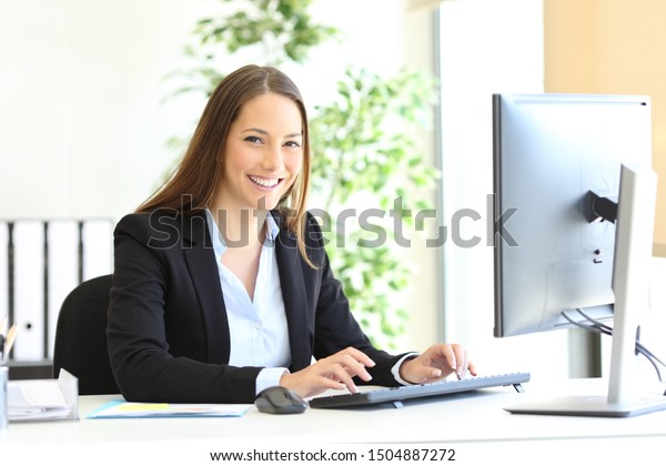 Happy executive looks at camera at office with the hands on computer keyboard at office