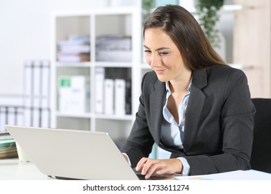 Happy executive woman working on laptop sitting on a desk at the office - Powered by Shutterstock
