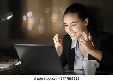 Happy executive working in the night crossing fingers checking laptop - Powered by Shutterstock