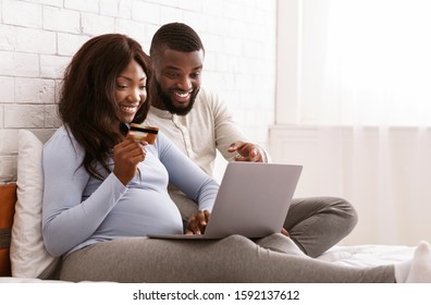 Happy expectant afro couple shopping online, using laptop and credit card, free space - Shutterstock ID 1592137612