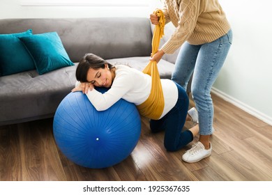 Happy expectant mother smiling while her doula lifts her pregnant belly with a rebozo. Hispanic doula helping a woman with her back and pelvis pain