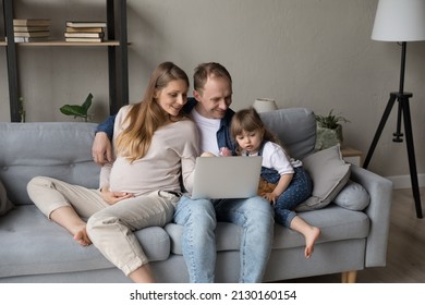 Happy Expecting Parents And Little Daughter Kid Relaxing On Couch Together, Watching Online Movie On Laptop, Enjoying Internet TV, Making Video Call. Pregnant Mom Holding Big Tummy. Family Leisure