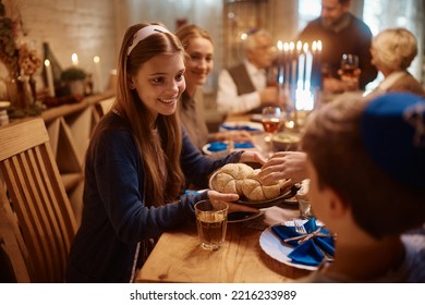 Happy Extended Family Celebrating Hanukkah While Having Dinner Together At Dining Table. Focus Is On Teenage Girl Passing Food To Her Brother.