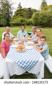 Happy Extended Family Having Dinner Outdoors At Picnic Table Smiling At Camera