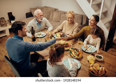 Happy Extended Family Having Dinner At Dining Table At Home. Focus Is On Young Woman Passing Food To Her Husband. 