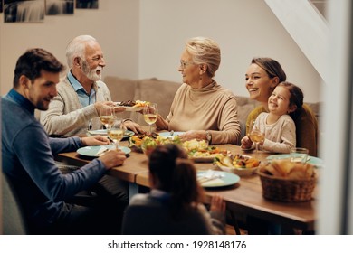 Happy Extended Family Having A Meal Together In Dining Room. Focus Is On Mature Couple Passing Food To Each Other. 