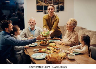 Happy extended family having a meal together at dining table. Focus is on young woman bringing salad at the table.  - Powered by Shutterstock