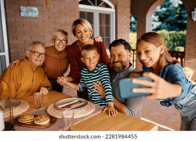 Happy extended family taking selfie while gathering for meal on a terrace. - Powered by Shutterstock