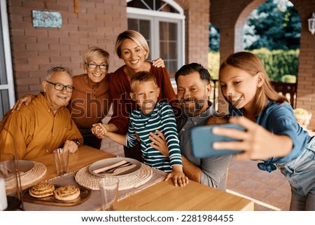 Happy extended family taking selfie while gathering for meal on a terrace.
