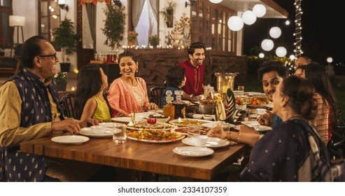 Happy Extended Indian Family Dining Together Outdoors in Fancy House Garden at Night. Family Members Laughing and Sharing Funny Stories and Memories While Eating Delicious Food
