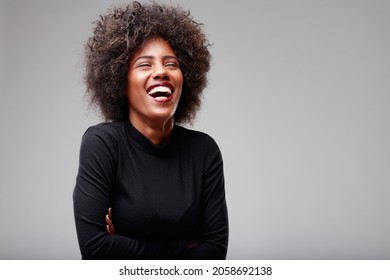 Happy exuberant young Black woman enjoying a good laugh as she poses with folded arms and head tilted back over a grey background with copyspace