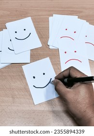 Happy face drawn on paper over sad face papers. Positive attitude concept. 