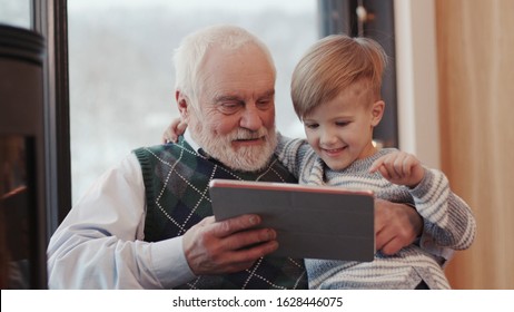 Happy Face Grandfather And Grandson Using Digital Tablet For Surfing Internet And Playing Game Near The Fireplace At Home Grandpa Adult Grandchild Child Childhood Communication Computer