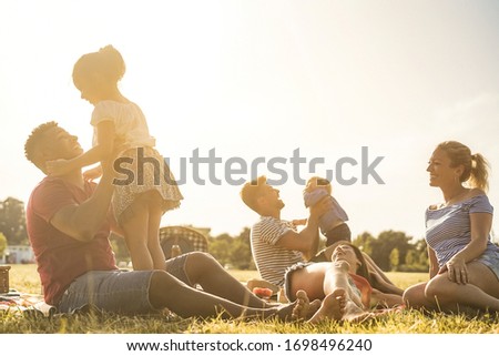 Happy families doing picnic in nature park outdoor - Young parents having fun with children in summer time laughing together - Positive mood and food concept - Soft focus on faces