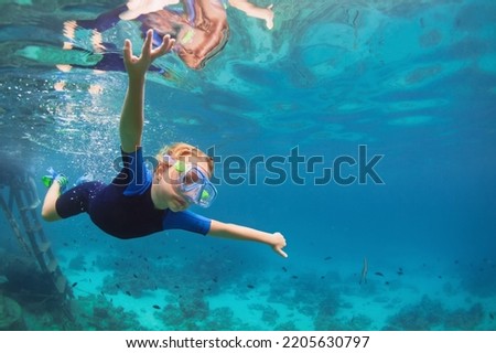 Happy family - active kid in wetsuit and snorkeling mask dive underwater, see tropical fishes in coral reef sea pool. Travel adventure, swimming activity on summer beach vacation with child.