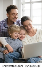 Happy Family With Adopted Kids Having Fun Using Laptop Together Sitting On Sofa, Parents And Son Daughter Relaxing At Home With Computer, Smiling Couple With Children Watching Video Online, Vertical