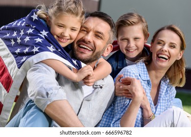 Happy family with american flag hugging outdoors, Independence Day concept