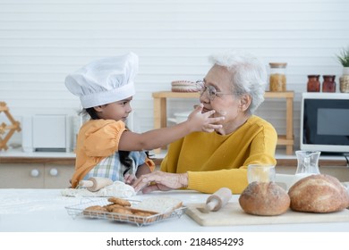 Happy family Asian grandmother and little grandchild spend time together at kitchen, knead dough and bake cookies or bread, niece have fun to tease and put flour on her grandma face at home - Powered by Shutterstock