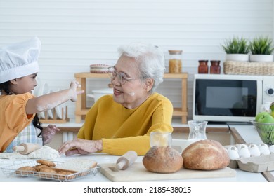 Happy family Asian grandmother and little grandchild spend time together at kitchen, knead dough and bake cookies or bread, niece have fun to tease and put flour on her grandma face at home - Powered by Shutterstock