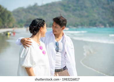 Happy family Asian on summer holiday vacation. Smiling senior couple holding hands and walking together on beach in sunny day. Healthy retirement people relax and enjoy outdoor lifestyle activity
