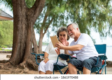 Happy Family Asian Senior Couple Using Tablet Computer With Internet Video Call With Their Family Or Friend On The Beach In Summer Day. Healthy Retired Man And Woman Enjoy With Summer Holiday Vacation