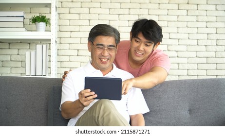 Happy Family Asian Two Generation Men. Grown Son Teaching Old Senior Father Use Digital Tablet Online Shopping Social Media At Home. Young Man Explain Mature Dad Learning Web Browsing Check Email.