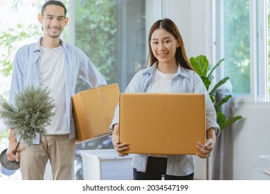 Happy family asian young wife and husband or couple holding carton parcel, carry cardboard box, plant pot for preparing moving relocation, new home, apartment. Mortgage, real estate for house owner.