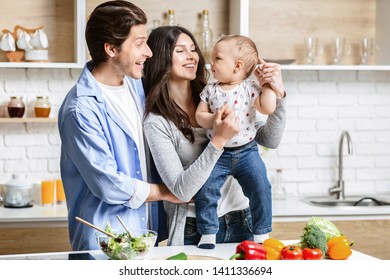 Happy Family With Baby Preparing Vegetable Salad In Kitchen, Free Space