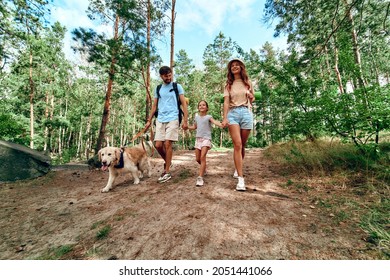 Happy family with backpacks and labrador dog are walking in the forest. Camping, travel, hiking.