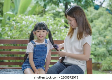 Happy Family Beautiful Mother Woman Brushing Her Daughter Hair While Sitting Outdoor At Home, Asian Smiling Child Schoolgirl With Long Dark Hair And Her Mom In The Morning, Hairstyle Care Concept