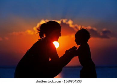 Happy Family Black Silhouette On Sunset Sky Background. Young Mother, Baby Son Have Fun Together, Walk By Sea Beach. Barefoot Child Look At Sun. Travel Lifestyle, Parents With Kids On Summer Vacation.