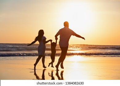 Happy Family Black Silhouette On Sun Background. Father, Mother, Baby Son Run. Child Jump With Fun By Water Pool Along Sea Surf On Beach. Travel Lifestyle, Parents Walking With Kid On Summer Vacation.