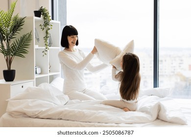 Happy family bonding moment with laughter and joy captured in natural light. Mother and daughter enjoying playful pillow fight in cozy bedroom. Bedtime fun and cheerful interaction, mom and child. - Powered by Shutterstock