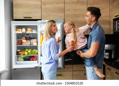 Happy Family With Bottle Of Juice Near Refrigerator In Kitchen