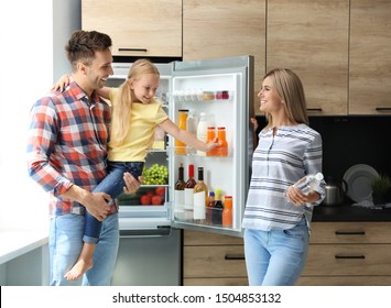 Happy Family With Bottle Of Water Near Refrigerator In Kitchen